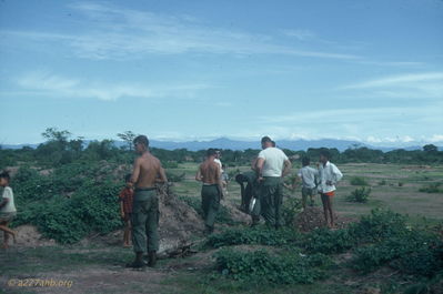 Searching for Crickets
Jim Puhala Photo

The kids would stage cricket fights. Theyâ€™d get a couple of crickets, rile them up by jabbing them with twigs and let them go after each other. The photo has the kids, with some help from SP4 Guinn, WO Hosmun and others searching for some new combatants.
This photo was taken at Song Mau. We spent a lot of time there - waiting. Weâ€™d put out a recon patrol in the morning. Theyâ€™d recon for a while; if they didnâ€™t find anything, weâ€™d pick them up and put them someplace else. If they did find s
